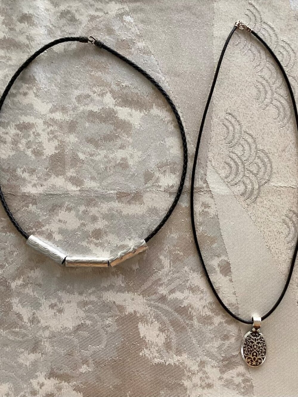 Two (2) silver and black cord necklaces, one with silver pendant, 19 inches